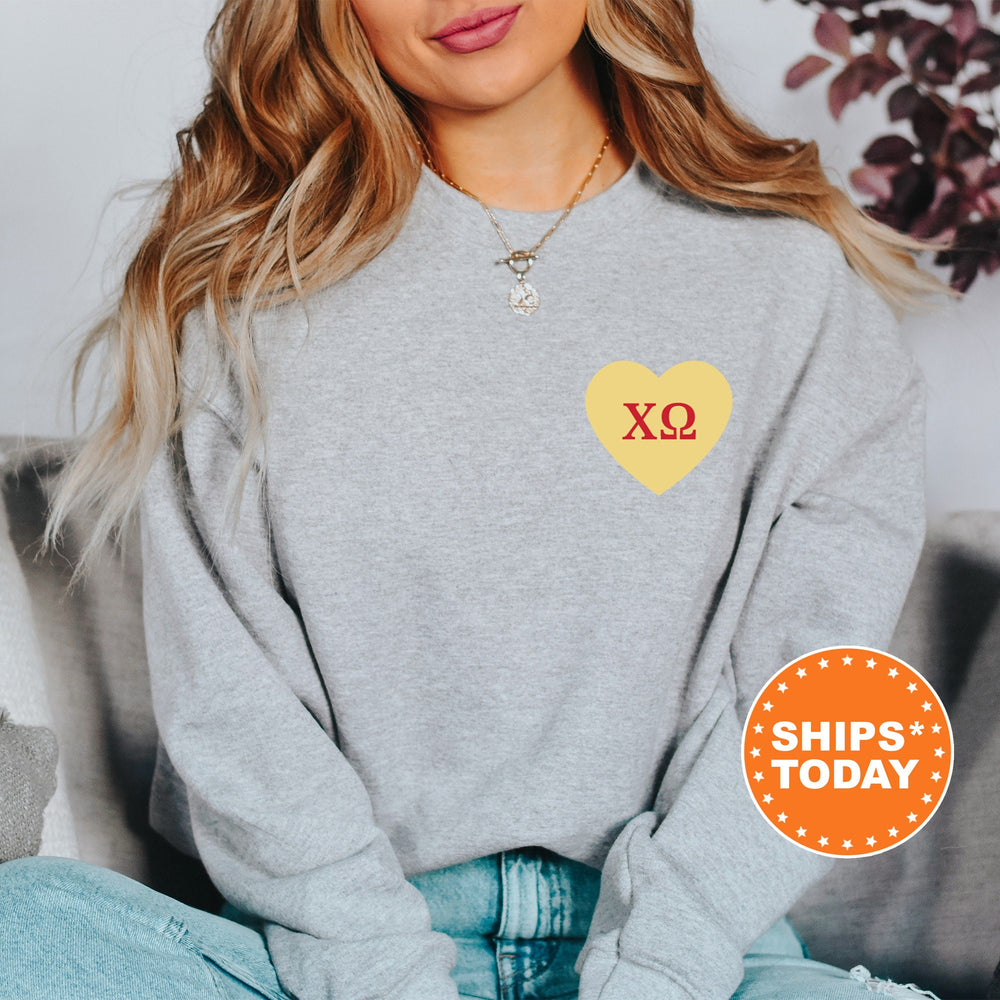a woman sitting on a couch wearing a grey sweatshirt with a yellow heart on it